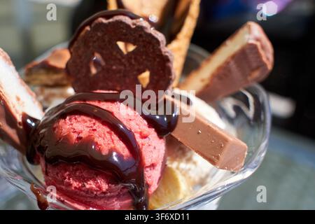 Un gros plan d'un sundae gourmet mettant en vedette des boules de framboise vibrantes trempées dans un riche sirop de chocolat, garni de divers biscuits, gaufrettes Banque D'Images