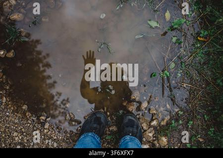 Person regardant son reflet agitant la main dans une flaque Banque D'Images