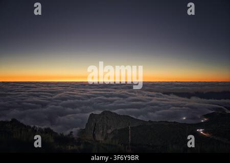 Juncal, Portugal - 05.12.2025 : Inversion de nuages blancs denses remplissant une vallée sous un sommet rocheux sombre à l'aube Banque D'Images