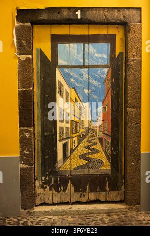 Funchal, Portugal - 05.12.2025 : Porte en bois artistique représentant une scène de rue traditionnelle avec des bâtiments lumineux et un pavage en pierre à motifs Banque D'Images