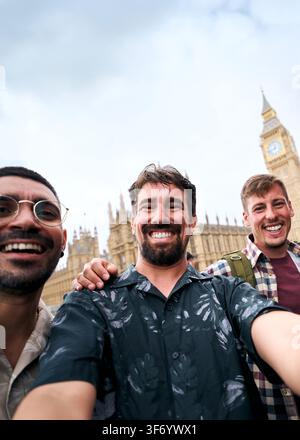 Trois amis hommes prenant un selfie avec Big Ben et un bus rouge lors d'un voyage en ville à Londres Banque D'Images