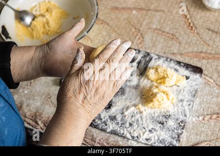 Un gros plan de mains âgées façonnant la pâte en petites galettes rondes pour préparer des syrniki traditionnels, illustrant une scène culinaire nostalgique axée sur l'artisanat Banque D'Images