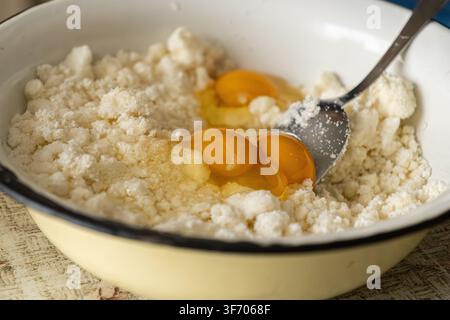 Close-up d'œufs frais cassés dans du fromage à pâte molle pour la préparation traditionnelle des syrniki, évoquant un sentiment de cuisine maison saine pendant une expérience culinaire Banque D'Images