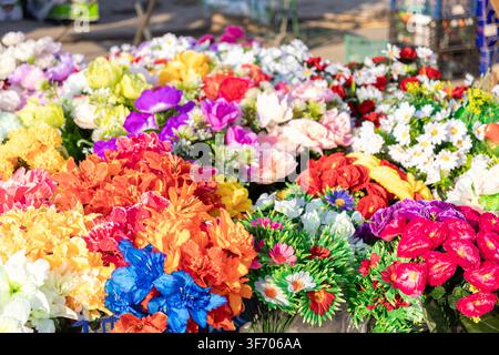 Collection variée de fleurs en soie colorées arrangées sur un marché de rue ensoleillé, représentant une esthétique festive et décorative pour les projets de design floral Banque D'Images