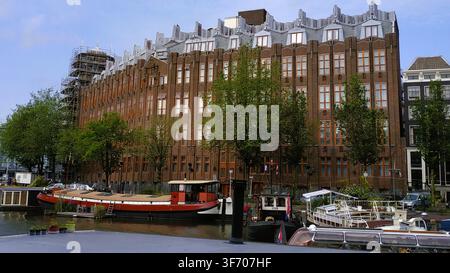Façade classique en briques reflétée sur les eaux du canal avec des péniches amarrées à Amsterdam, Pays-Bas Banque D'Images
