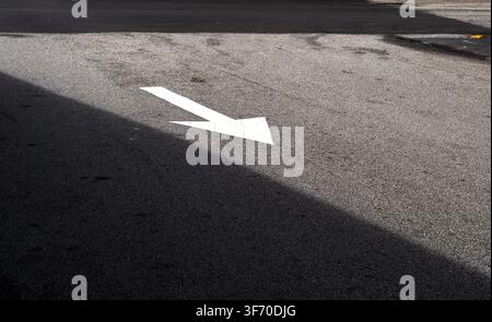 Flèche directionnelle blanche peinte sur la surface de la route en asphalte avec contraste d'ombre Banque D'Images