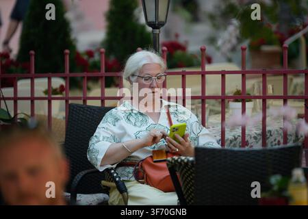 Une femme portant des lunettes à la mode est vue utilisant son téléphone portable dans un restaurant à Varsovie, Pologne, le 4 août 2026, alors qu'une vague de chaleur s'empare du pays. Les températures dans la capitale polonaise devraient atteindre 34°C mardi et monter à 37°C mercredi, avec des parties du sud-est de la Pologne prévoyant des pics jusqu'à 39°C, selon l'Institut de Météorologie et de Gestion de l'Eau (IMGW). (Photo par Jaap Arriens / Sipa USA) Banque D'Images