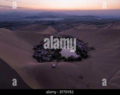 Vue aérienne de l'oasis de Huacachina entourée de vastes dunes de sable au coucher du soleil à Huacachina, Ica, Pérou. Banque D'Images