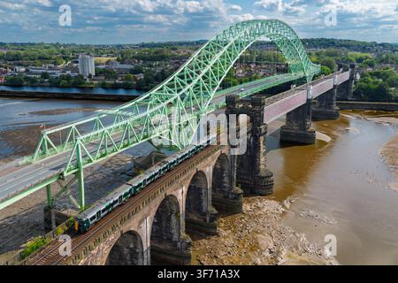 Un train traversant le viaduc victorien au-dessus de la rivière Mersey en direction de Runcorn avec le pont routier Queensway à gauche. Banque D'Images