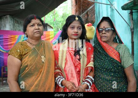 Mariée bengali indienne en saree rouge debout avec deux femmes âgées, membres de la famille, pendant la cérémonie de mariage au Bengale occidental Banque D'Images