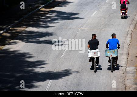 Deux cyclistes pédalant avec des caisses côte à côte à Ciego de Avila, Cuba - 26 juillet 2026 Banque D'Images