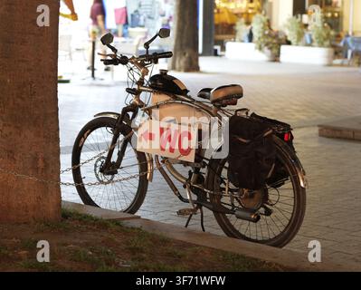 Vélo motorisé doté d'un panneau directionnel de toilettes improvisé attaché à son cadre, garé la nuit sur un trottoir urbain à côté d'un arbre, suggérant une qui Banque D'Images