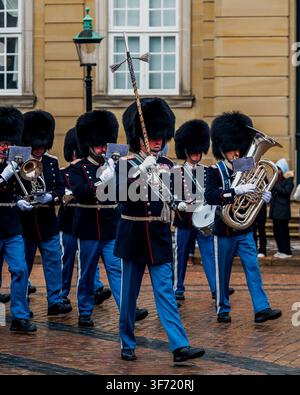 Copenhague, Danemark – décembre 2025 : Membres d’une fanfare militaire danoise coiffés de chapeaux en peau d’ours marchent devant le palais d’Amalienborg en jouant des instruments à vent en laiton et dr Banque D'Images