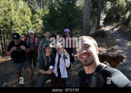 Novembre 2023 : Un groupe d'amis et un chien posent pour un selfie pris par un randonneur sur un sentier forestier ensoleillé. Banque D'Images