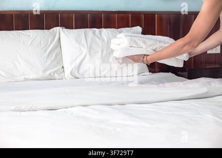 Hôtelière posant des serviettes blanches soigneusement pliées sur un lit fraîchement fait. Service d’hôtellerie, chambre d’hôtel propre, housekeeping professionnel. Banque D'Images