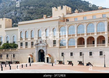 Monaco, Monaco - 17 juillet 2026 : Un carabinier princier se tient devant l'entrée principale du palais princier de Monaco, avec des canons historiques sur Pala Banque D'Images