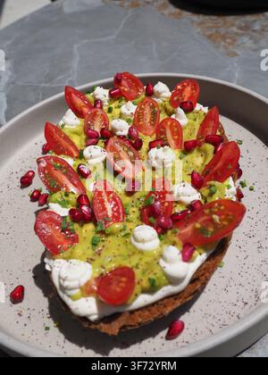 Gros plan d'un toast à l'avocat avec des tomates cerises, des graines de grenade et de la crème fraîche sur un pain au levain rustique Banque D'Images