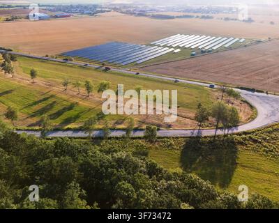 Vue aérienne d'une ferme solaire avec des rangées de panneaux photovoltaïques situés dans un paysage rural avec une route sinueuse, des arbres et des champs à Viglas, Banska By Banque D'Images