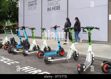 Les piétons passent devant des scooters électriques locatifs Lime et Dott garés pour le transport urbain devant One New Change dans la City de Londres. Banque D'Images