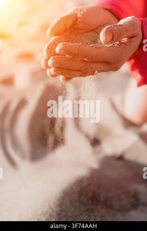 Mains laissant tomber du sable entre les doigts sur une plage ensoleillée, représentant le concept du temps qui passe et de la liberté Banque D'Images