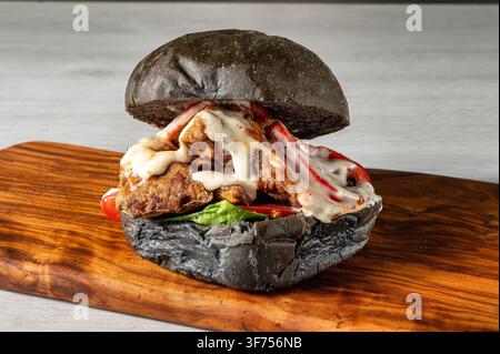 Burger maison avec pain au charbon de bois, poulet frit croustillant, laitue iceberg, tomate, sauce aïoli crémeuse et citron vert, présenté sur une planche en bois Banque D'Images