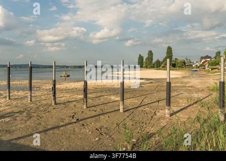 Niveau d'eau bas au lac de Constance : Bateaux échoués sur un lit sec à côté d'un ponton en bois pendant une sécheresse estivale à Berlingen, Suisse. Banque D'Images