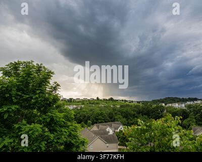 Les rayons du soleil crépusculaires percent un front orageux sombre et dramatique qui s'annonce au-dessus d'une ligne d'arbres suburbaine verdoyante en Pennsylvanie. Banque D'Images