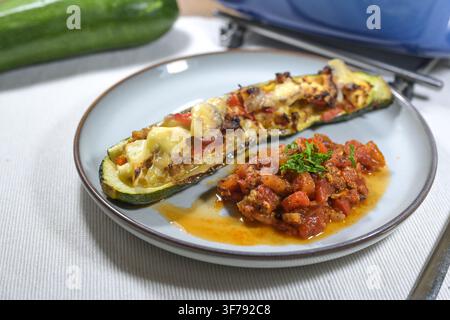 Courgette mi-cuite au four, farcie de poivron, thon, oignons et feta, servie sur une assiette avec une salsa de tomates et une garniture de persil, plat sain pauvre en glucides Banque D'Images