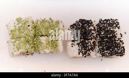 Rollés de sushi Uramaki recouverts de graines de sésame vertes et noires sur un fond blanc propre Banque D'Images
