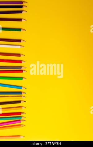 Une rangée de crayons de couleur est posée sur un fond jaune. Les crayons sont alignés soigneusement, montrant diverses couleurs pour les fournitures scolaires. Cette scène se pr Banque D'Images