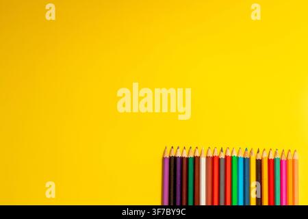 Des crayons de différentes couleurs reposent sur une surface jaune vif. Ils sont alignés soigneusement, prêts pour les activités scolaires. Parfait pour les projets artistiques et les devoirs Banque D'Images