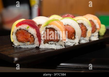 Un gros plan, une photographie alimentaire de style de vie à faible angle mettant en valeur un rouleau de sushi arc-en-ciel premium rempli de thon épicé haché, magnifiquement garni d'alter Banque D'Images