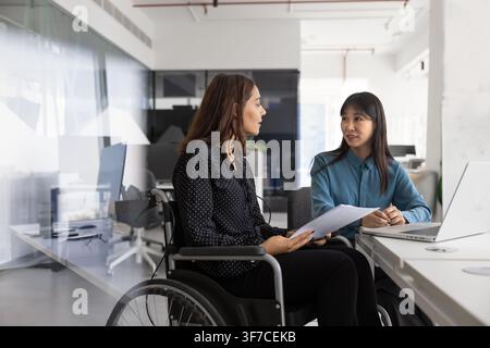 Jeune femme assise en fauteuil roulant, en discussion avec un collègue Banque D'Images