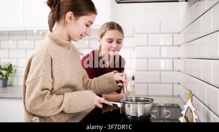 Les sœurs font fondre des ingrédients sur la cuisinière, préparant des biscuits gingersnaps pour une célébration de Noël Banque D'Images