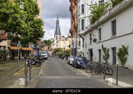 Lyon, France - 27 juillet 2026 : Rue pavée du Vieux Lyon avec voitures garées, vélos et flèche d'église en arrière-plan. Banque D'Images