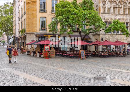 Lyon, France – 27 juillet 2026 : Terrasse extérieure de restaurant avec parasols rouges et sièges sur une place pavée dans le quartier historique de Vieux Lyon. Banque D'Images