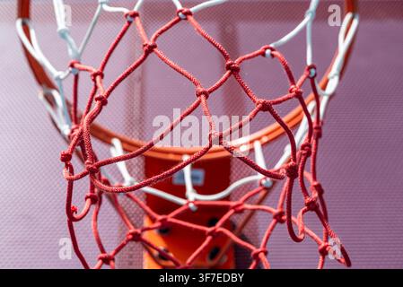 Plan rapproché d'un terrain de streetball urbain montrant un panier de basket rouge et un panneau arrière en métal perforé Banque D'Images