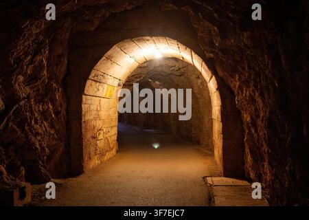 Un arc ancien magnifiquement illuminé se dresse dans un tunnel sombre, créant une atmosphère mystérieuse et historique. La vue frontale met en valeur la pierre s Banque D'Images
