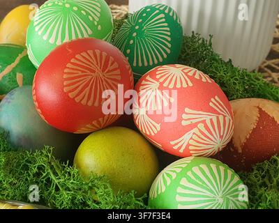 Un arrangement en gros plan d'œufs de Pâques colorés peints à la main, disposés sur de la mousse verte. Les œufs présentent différentes couleurs, dont du rouge vif, du corail Banque D'Images