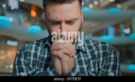 Close up d'un homme caucasien pliant les mains en prière les yeux fermés souhaitant l'espoir à l'intérieur. Portrait d'un homme priant espérant souhaitant le pardon religieux spirituel Banque D'Images