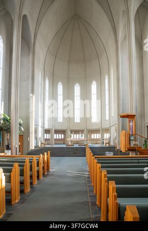Vue verticale saisissante de la nef centrale de l'église Hallgrímskirkja à Reykjavik, avec des bancs en bois proéminents au premier plan, une haute pile en béton Banque D'Images