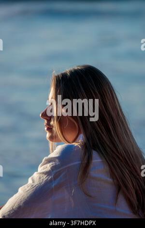 Femme contemplant une eau calme, trouvant la paix et la tranquillité à l'heure dorée Banque D'Images