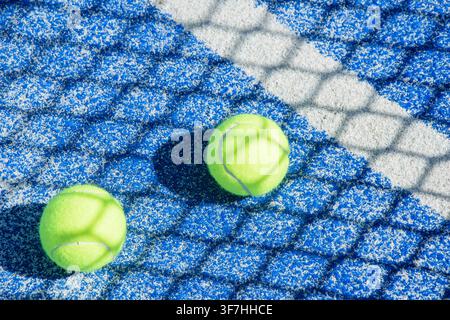 Vue de dessus de deux balles de padel jaunes reposant sur un court en gazon synthétique bleu avec une ligne de limite blanche Banque D'Images