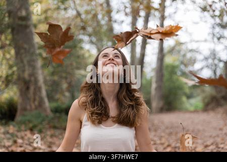 Femme heureuse profitant des feuilles d'automne qui tombent dans la forêt Banque D'Images