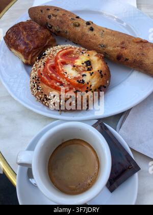 Un plan par-dessus montre une tasse d'espresso avec une crème épaisse, servie à côté d'une assiette blanche remplie de pâtisseries : une pâtisserie salée à la tomate et Banque D'Images