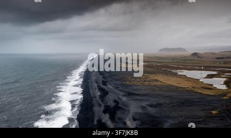 Plage de sable noir de Reynisfjara depuis le point de vue de la péninsule de Dyrholaey. Paysage côtier plage de sable volcanique noir vagues de l'océan Atlantique ciel menaçant Islande ic Banque D'Images