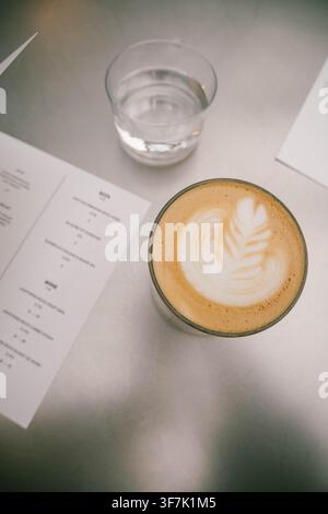 Vue de dessus d'un latte avec une décoration en mousse en forme de feuille à côté d'un verre d'eau et de menus de café Banque D'Images