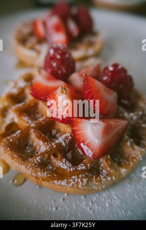 Close-up de gaufres maison garnies de fraises et framboises fraîches, de sirop et de sucre en poudre pour le petit-déjeuner Banque D'Images