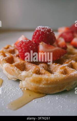 Close-up de gaufres maison garnies de fraises et framboises fraîches, de sirop et de sucre en poudre pour le petit-déjeuner Banque D'Images