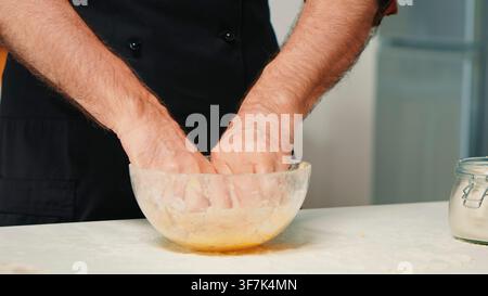 Chef à la retraite portant un tablier plie et presse une pâte maison dans le cadre de la préparation pratique des aliments, dans une zone de préparation de recettes domestique pendant la préparation de la pâte. Banque D'Images